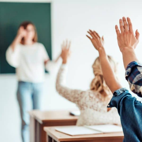 rear view of group of students raising hands in class on lecture