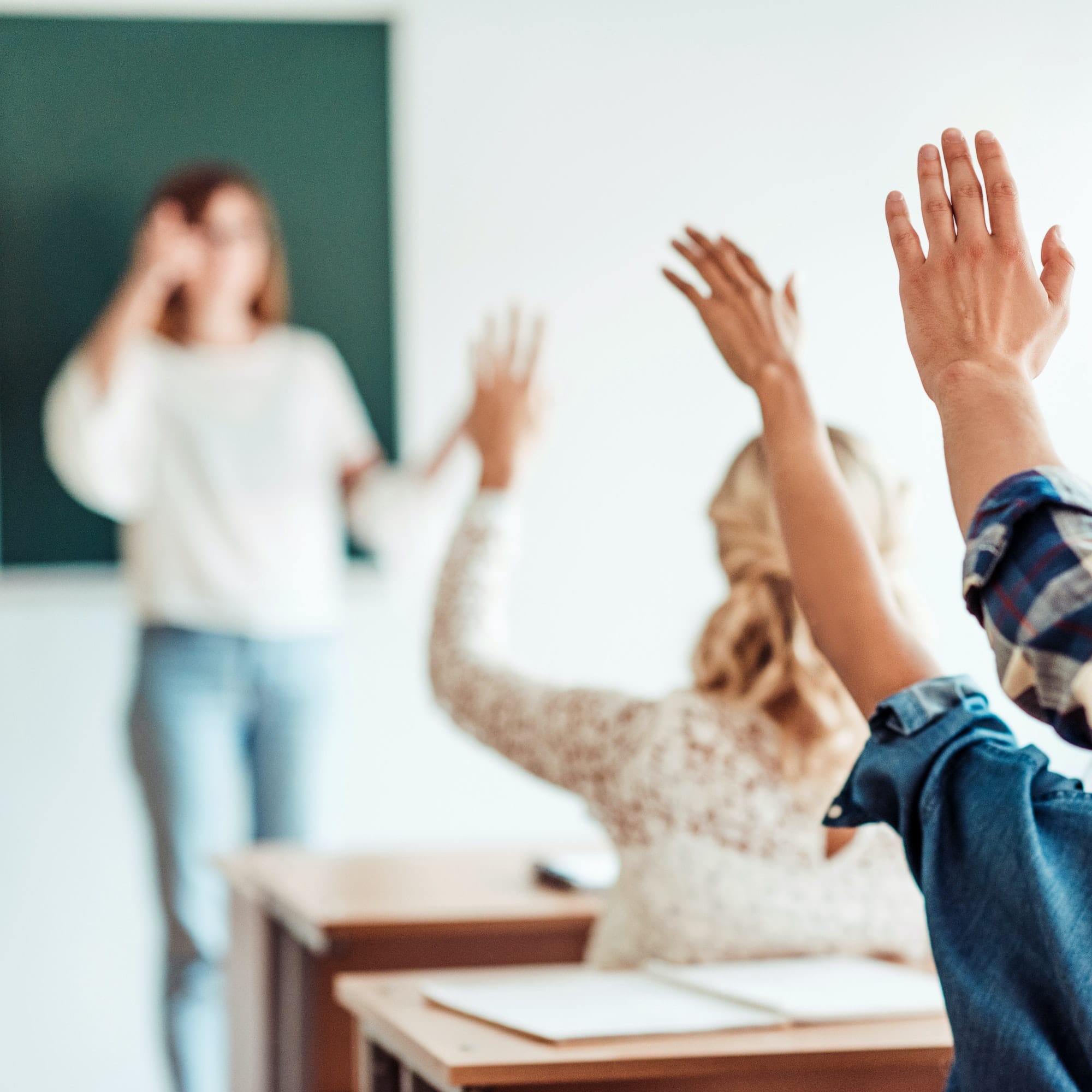 rear view of group of students raising hands in class on lecture